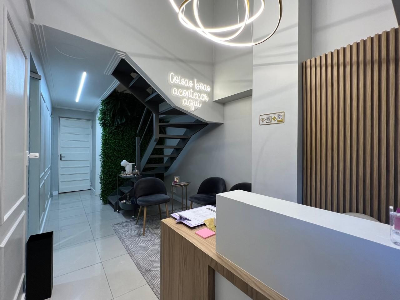 Recepção com balcão branco e madeira, corredor iluminado e escada ao fundo