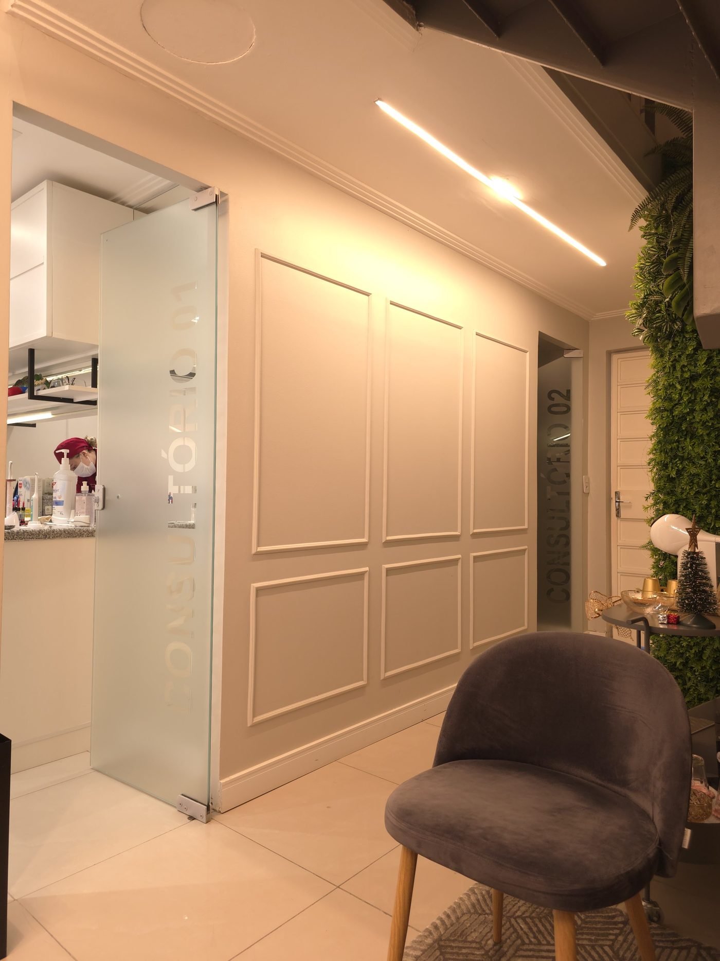 Sala de espera com poltrona de veludo, paredes com boiserie e o jardim vertical ao lado