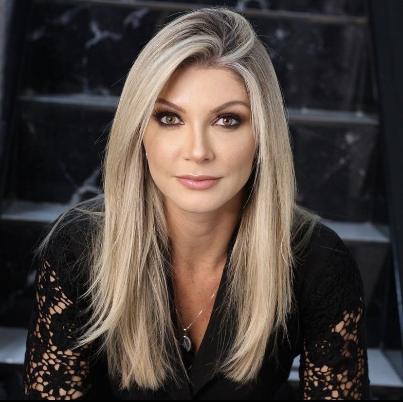 Dra. Camille van der Broocke, de blusa preta de renda, diante de uma parede de mármore escuro