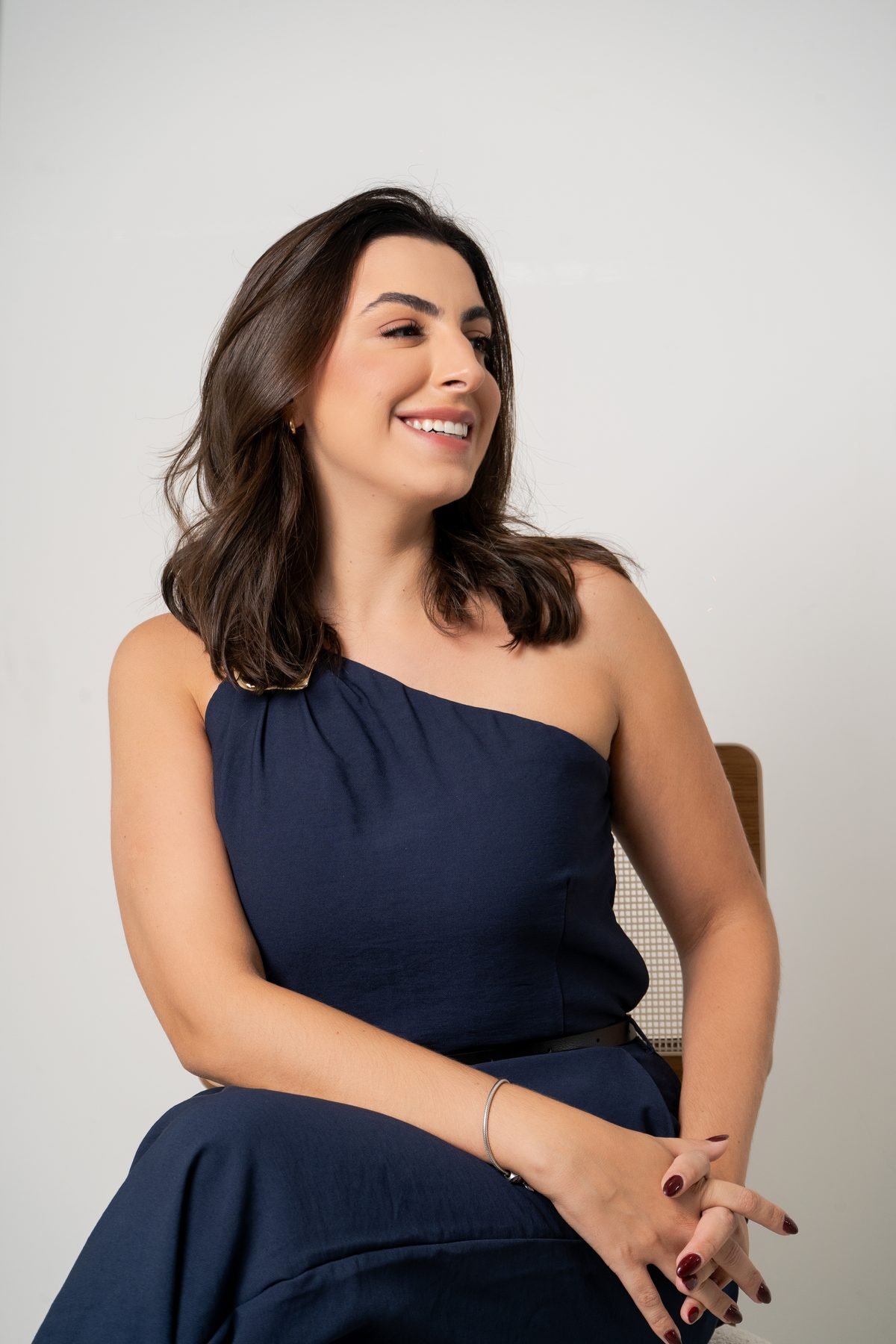Dra. Gabrielle sentada, de vestido azul-marinho, sorrindo